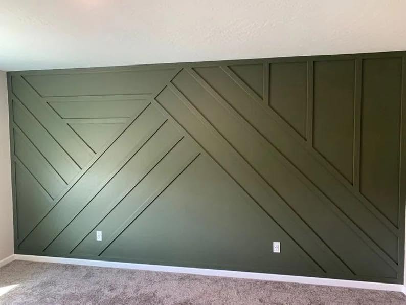 An interior wall clad in angled wood trim forming a repeating geometric pattern, painted deep olive green.